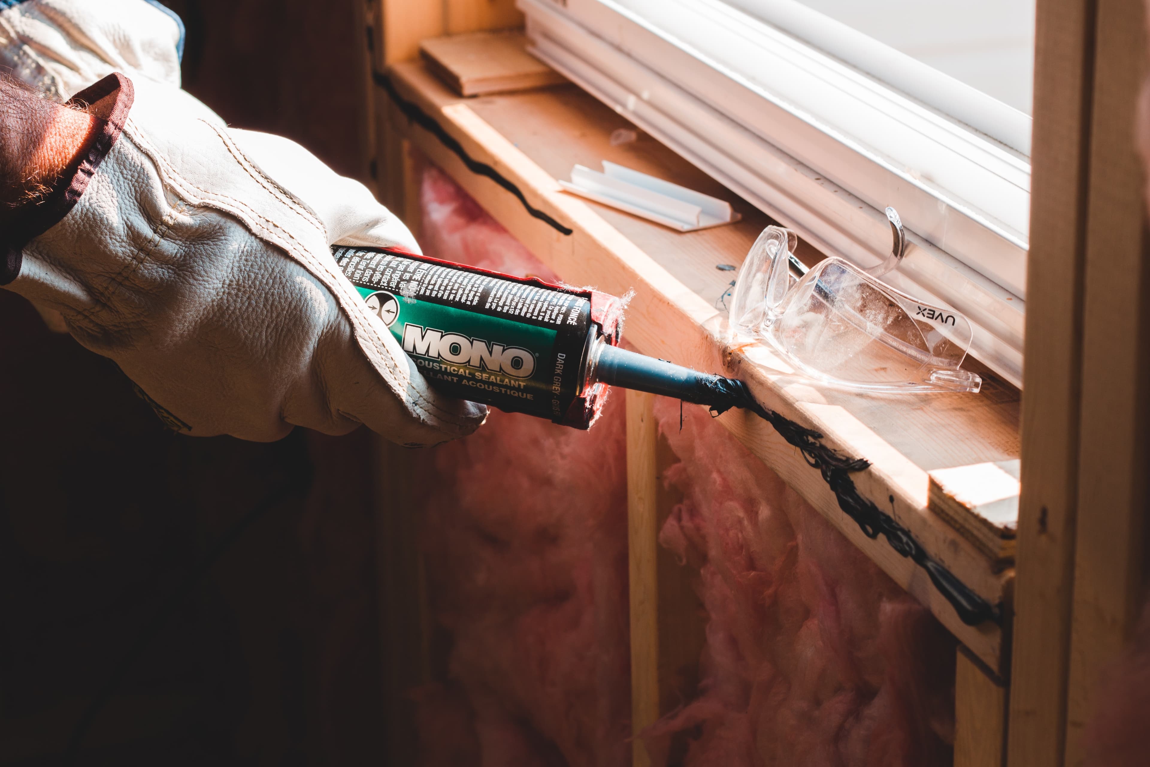 A builder applying acoustical caulk to a window